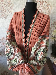 an orange crocheted sweater on a mannequin's head with hands in the air