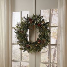 a wreath hanging on the side of a door with pine cones and evergreens around it