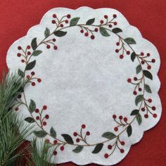 a white doily with red berries and green leaves on it next to a pine tree