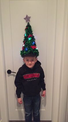 a young boy standing in front of a door wearing a christmas tree hat