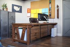 a wooden desk sitting in the middle of a room next to a filing cabinet and refrigerator