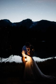 a bride and groom standing in front of a lake at night