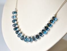 This sumptuous necklace would be the perfect "something blue" for a bride-to-be! The fine-cut facets of the midnight blue teardrops contrast beautifully with the lustrous white pearls. The elegant curve of the necklace would work well with a sweetheart, strapless, or scooped neckline.   Micro-faceted London Blue Topaz teardrops are combined with white freshwater pearls and fine sterling silver chain. Necklace is finished with a sterling silver spring clasp and a 2.5" adjustable chain. Necklace m Blue Gemstone Wedding Necklace, Wedding Necklace In Sapphire Blue Topaz, Blue Briolette Necklace For Wedding, Blue Briolette Pearl Necklace For Gift, Blue Topaz Necklace For Wedding, Blue Gemstone Beads Necklace For Wedding, Blue Briolette Necklace For Anniversary, Wedding Blue Topaz Faceted Jewelry, Gift Blue Briolette Pearl Necklace