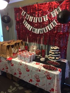 a table topped with lots of cakes and desserts next to a red curtain covered wall