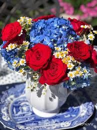 red, white and blue flowers are in a vase on a table with china plates