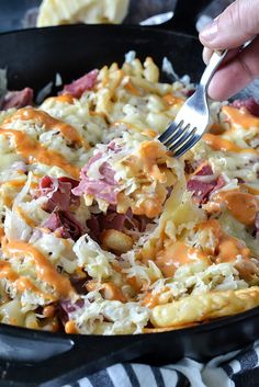 a person holding a fork in a skillet filled with macaroni and cheese