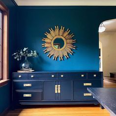 a room with blue walls and wooden floors has a gold sun mirror on the wall