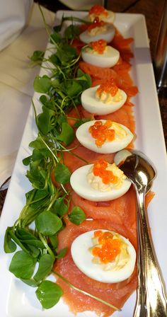 an assortment of deviled eggs and greens on a white platter with a spoon