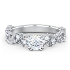 a white gold engagement ring with an intricate design on the band and a round diamond center stone