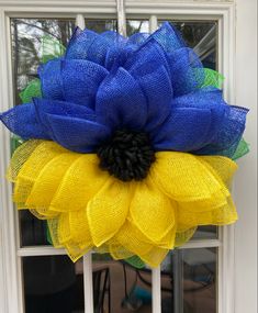 a blue and yellow mesh wreath with a flower on the front door window sill