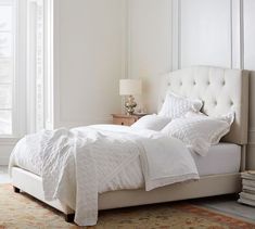 a bed with white linens and pillows in a bedroom next to a large window