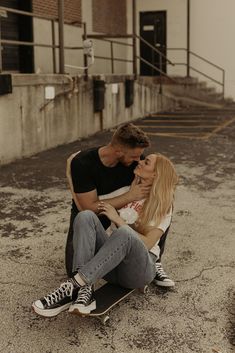 a man and woman sitting on top of a skateboard in front of a building