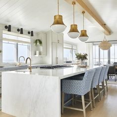 a large kitchen with marble counter tops and blue chairs in front of an island that has gold pendant lights hanging from the ceiling