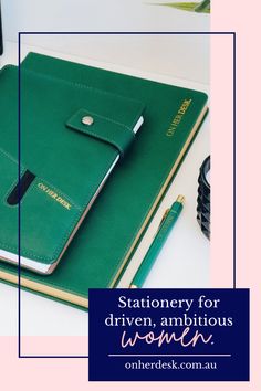 a green notebook sitting on top of a white desk next to a phone and pen