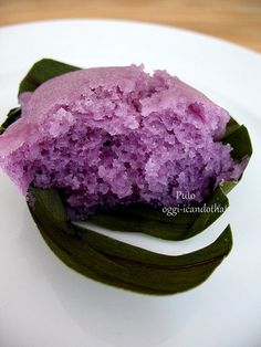 there is a small purple cake on the plate with green beans and leaves around it