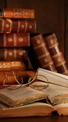 an open book with glasses on top of it next to some books and a pair of reading glasses