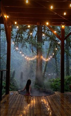 a woman sitting on top of a wooden deck next to a tree covered in lights