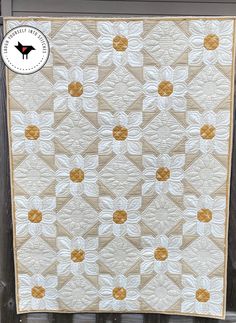 a white and gold quilt hanging on the side of a wooden fence with an orange border