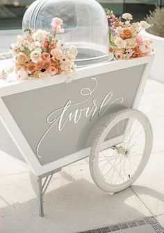 a white cart with flowers and a cake on the back that says, sweet in cursive writing