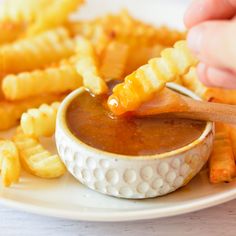 a person dipping sauce onto french fries on a plate