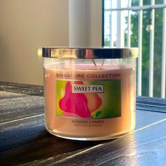 a pink candle sitting on top of a wooden table next to a glass window with the words sweet pea printed on it