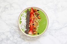 a green smoothie bowl with strawberries, nuts and other toppings on top