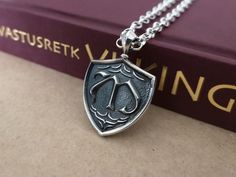 a book with a silver pendant on it sitting next to a chain that has the letter d on it