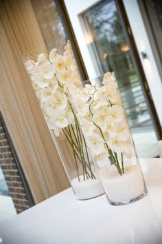 two tall vases filled with white flowers sitting on a table next to each other