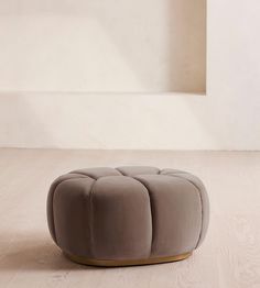 a round ottoman sitting on top of a hard wood floor next to a white wall