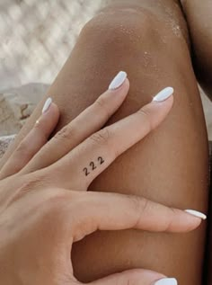 a woman with white nails and a small tattoo on her left hand is sitting in the sand