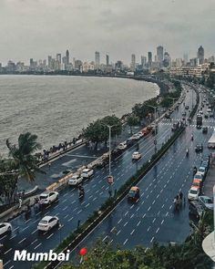 a city street filled with lots of traffic next to the ocean and tall buildings in the distance