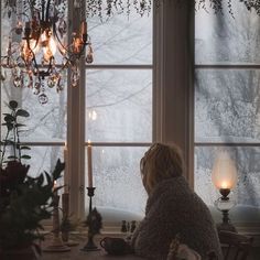 a woman sitting at a table in front of a window with a candle and some flowers