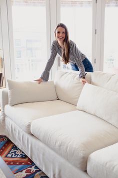 a woman standing on top of a white couch in a living room next to a window