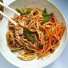 a white bowl filled with noodles, carrots and green peppers next to chopsticks