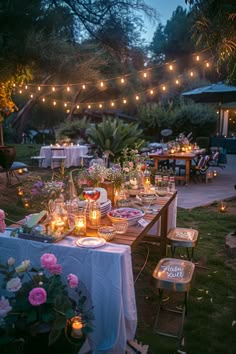 an outdoor dinner table set up with candles and flowers on the table, surrounded by string lights