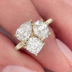 two pear shaped diamond engagement rings on someone's hand, with the middle one in yellow gold