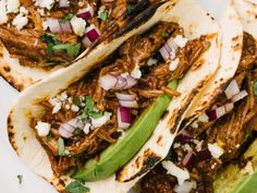 three tacos with shredded meat, onions and green peppers on them sitting on a white plate