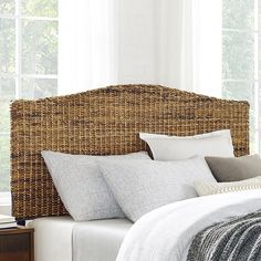 a wicker headboard with white linens and pillows on a bed in front of a window