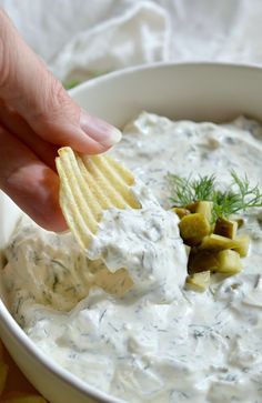 a hand dipping a cracker into a bowl of dip with potatoes and dill