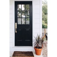 a black front door with two potted plants on the side and a brown rug