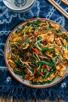 a plate full of stir fried vegetables with chopsticks next to it on a blue towel