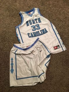 two white and blue basketball uniforms laying on the floor next to each other, one is wearing