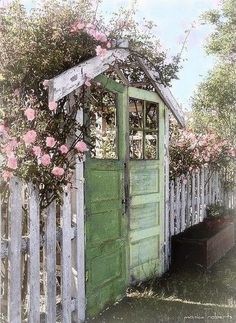 an old outhouse with flowers growing over it's roof and door, next to a white picket fence