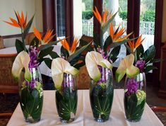 three vases filled with flowers sitting on top of a white tablecloth covered table