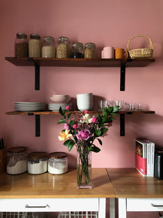 a vase with flowers sitting on top of a wooden table next to shelves filled with dishes