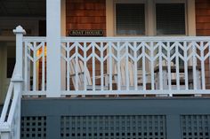 the front porch of a house with white railings and chairs on it's side