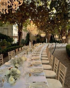 a long table is set with white linens and place settings for an elegant dinner