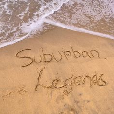 the word suburban legend written in sand at the beach with waves coming in to shore