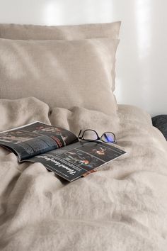 an open magazine laying on top of a bed next to eyeglasses and pillows