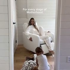 a woman sitting in a white chair next to a little boy on the floor near a door